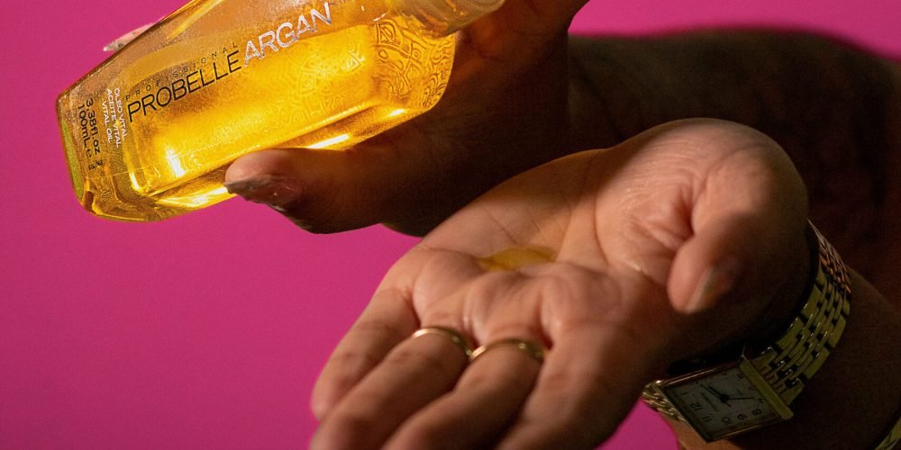 Hand holding a bottle of yellow Argan Oil hair , one of the best hair care products to treat dry hair.